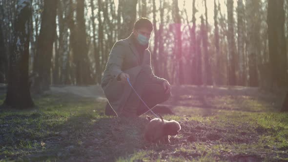 Man Squats and Stands Near Adorable Puppy Sniffing Grass