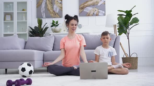  Woman Doing Yoga Exercises Together With Her Calm Teen Son in Front of the Laptop