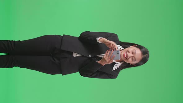 An Asian Business Woman Enjoy Using Mobile Phone While Standing On Green Screen In The Studio