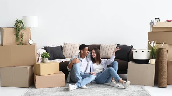 Happy Young Multiracial Couple Caucasian Woman and Hispanic Guy are Sitting on the Floor Between