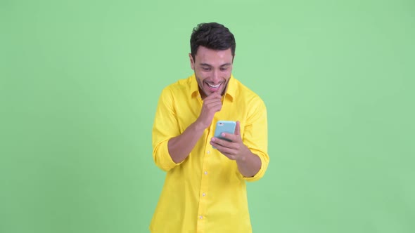 Happy Young Hispanic Businessman Using Phone and Looking Surprised