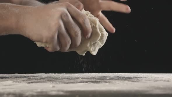 Male Hands Knead a Piece of Dough and Tears It in Half Above Wooden Table Sprinkled with Flour