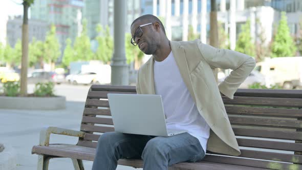 African Man with Back Pain Using Laptop While Sitting Outdoor on Bench