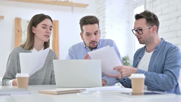 Angry Creative Team Arguing Over Documents and Working on Laptop