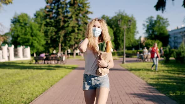 Caucasian Young Pretty Woman Delivery Worker in Medical Mask Walking the Street and Carrying Packet