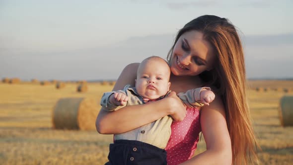 Portrait of a Little Baby Son in Mother Hands is Caressed in Spacious Hay Field