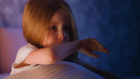 Upset Little Girl Wipes Nose and Tears on Bed at Moon Light