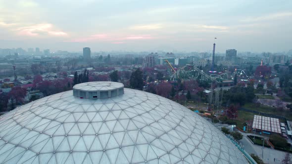 Aerial view dolly in of the ellipse and amusement park at O'Higgins Park, Santiago, Chile. Sunset wi