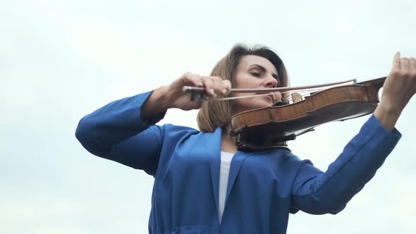 Woman Playing Violin Against Gray Sky