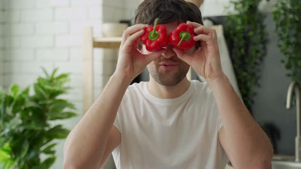 Happy Smiles and Plays Happily with Red Peppers in Front of His Eyes in the Home Kitchen