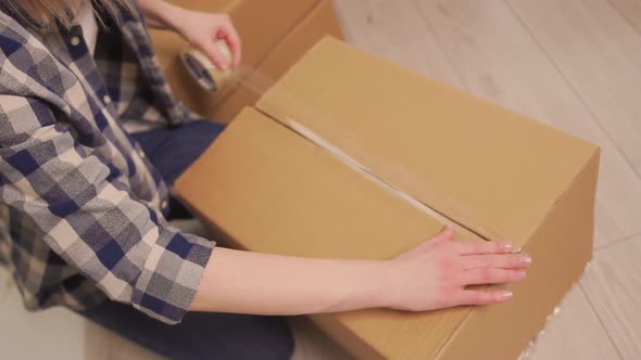 An Overhead View of the Woman Covers a Cardboard Moving Box with Duct Tape