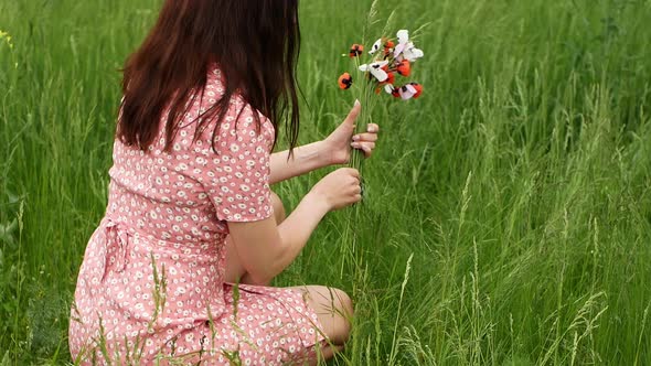 A woman in a beautiful dress collects a spring bouquet of flowers in a field with green grass.