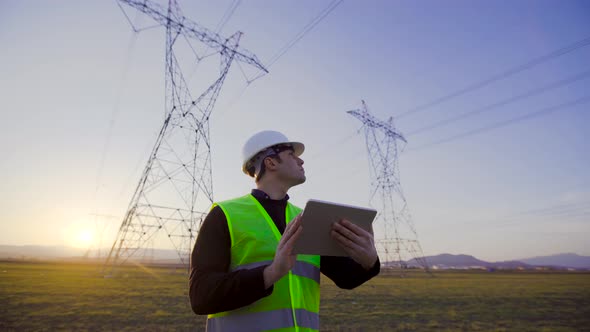 Engineer working in front of power lines at sunset.