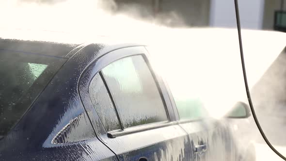 Car wash with high-pressure device. Stream of water in sun rays