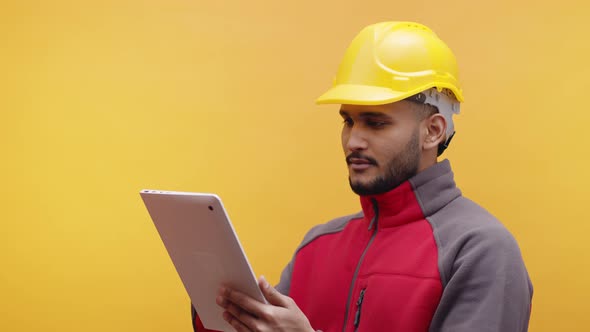 Young Indian Engineer with Yellow Helmet Using Tablet and Smiling