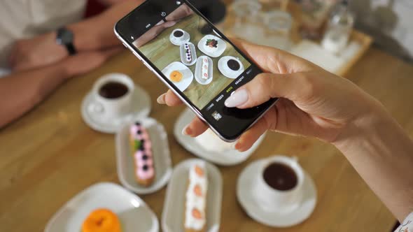 Woman Takes Picture of Tasty Cakes and Tea on Wooden Table