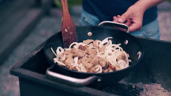 Close-up, Travelling Shot: Young Man Makes Pilaf, in a Cauldron, on a Grill, on an Open Fire