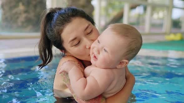 Happy Mother in Red Swimming Suit with Baby Son Surfing Water with Fun in Swimming Pool