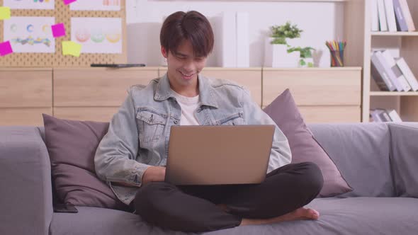 Enjoying the moment. At work, an Asian businessman sits at his desk with his laptop, tablet, and doc