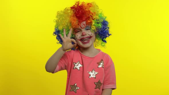 Little Child Girl Clown in Colorful Wig Making Silly Faces. Shows Ok Sign, Smiling. Halloween