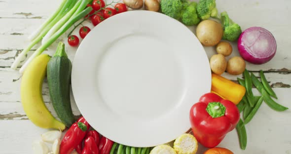 Video of fresh fruit and vegetables around white plate with copy space on wooden background