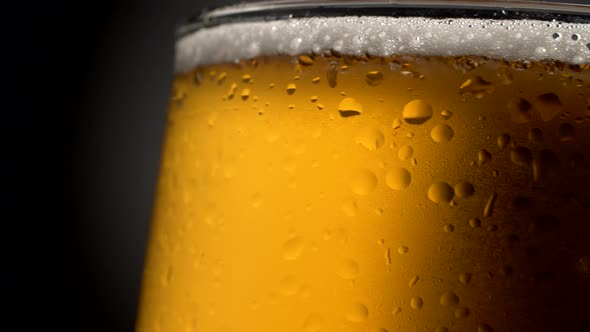 Beer Mug Close-up. Wet, Rotating Glass Filled with Golden-colored Cooled, Foamy Beverage on a Dark