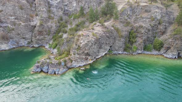 Aerial view of people jumping off cliff at rattlesnake point into turquoise water of  Kalamalka lake