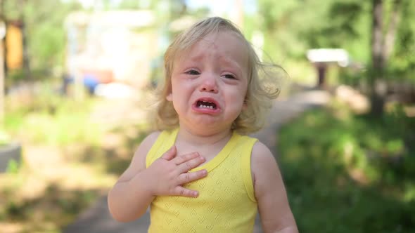 Close Up Portrait of Little Funny Cute Blonde Girl Child Toddler in Yellow Bodysuit Crying Outside