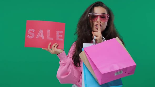 Smiling Beautiful Young Woman Showing Sale Sign and Holding Shopping Bags, Looking at Camera