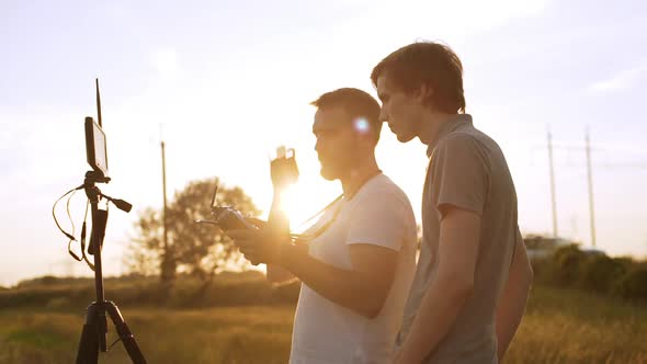 Two Men Standing Near Quadrocopter Screen Monitor on Tripod Shooting and Flying in Rural Area Wheat