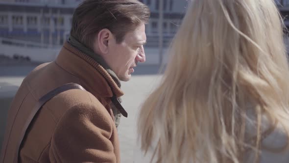 Portrait of Handsome Man and Pretty Blond Woman in Warm Jacket Sitting at the City Street Talking