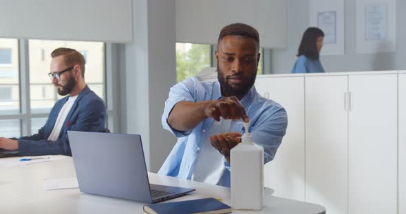 Portrait of Young Africanamerican Man Sanitizing Hands While Working in Office