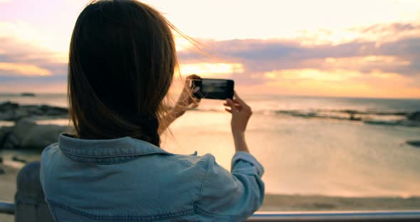 Woman clicking photos with mobile phone at beach