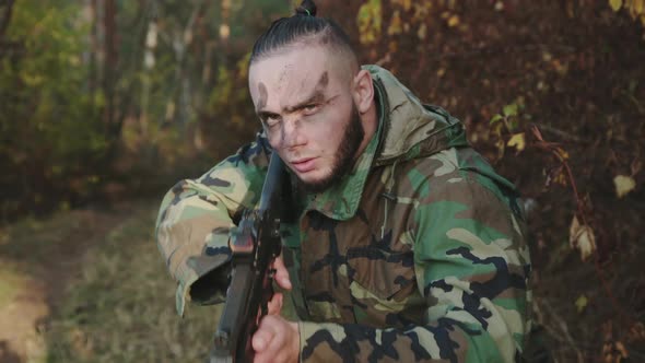 Portrait of Hunter with Soot Strips on Face Aims Gun at an Object in the Forest