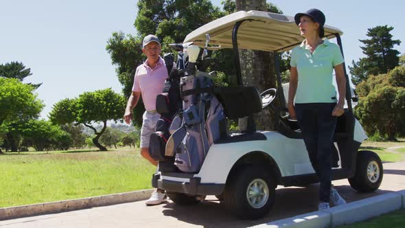 Caucasian senior couple removing golf clubs from back of a golf cart at golf course