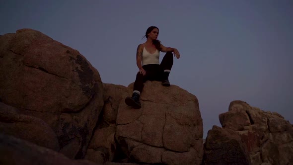 Girl sitting on the edge of a rock at Joshua Tree national park looking at sunset, slow motion