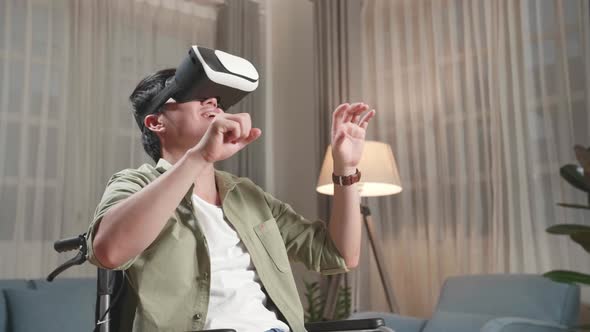 Funny Asian Man Sitting In A Wheelchair While Wearing Virtual Reality Goggles At Home