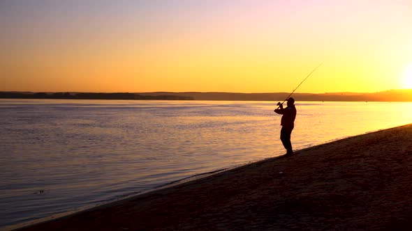 A Man Is Fishing at Sunrise By the River. The Yellow Sun Rises From the Horizon, Silhouette 