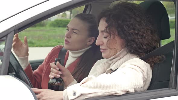 Two Girlfriends Drink Wine From a Bottle While Sitting in the Car