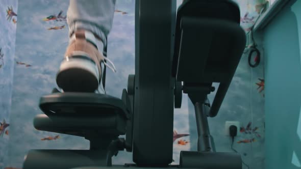 Young Girl in Sneakers is Engaged in an Orbitrek at Home Bottom View