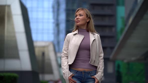 Unhappy Blonde Woman Is Walking Alone on City Street, Wrapping in Jacket at Cold Spring Day