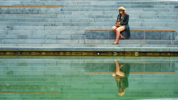 Sad Girl Chatting Smartphone Reflecting in Lake Water in Urban Park