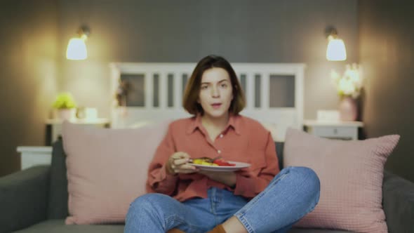 Young Woman Having a Dinner on the Couch in Front of the TV