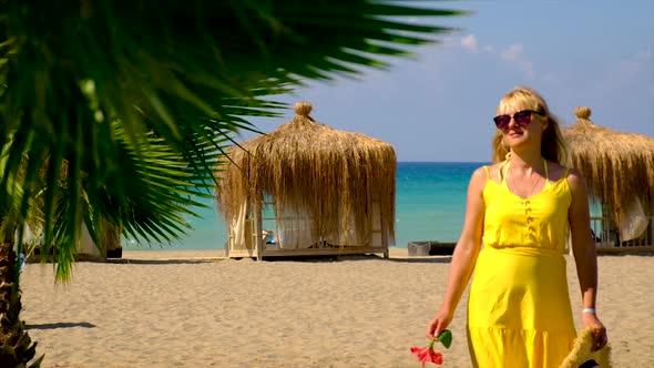 A Woman in a Hat and Dress Walks on the Beach