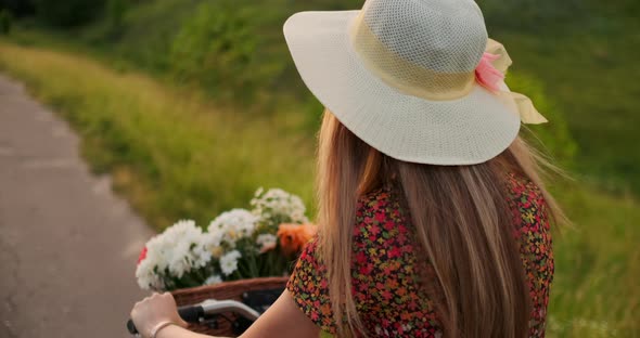 Happy Girl with a Bouquet of Flowers Riding a Bike in a Hat and a Summer Short Dress