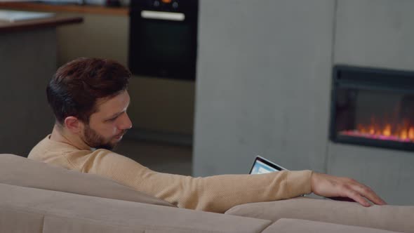 A man with a laptop on the couch by the fireplace