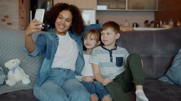 African American Woman Babysitter Taking Selfie with Adorable Kids at Home Using Smartphone Camera