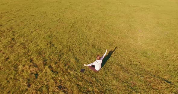 Low Orbital Flight Around Man on Green Grass with Notebook Pad at Yellow Rural Field