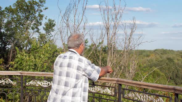 Old Man Walks Near Metal Railing Against Lush Green Nature