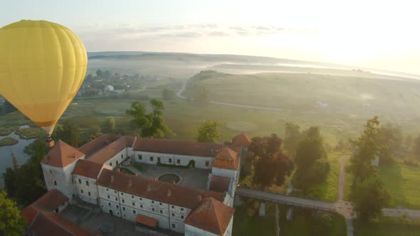 Colorful Hot Air Balloons Fly Over the Medieval Castle and Lake in the Morning Fog. Maneuverable